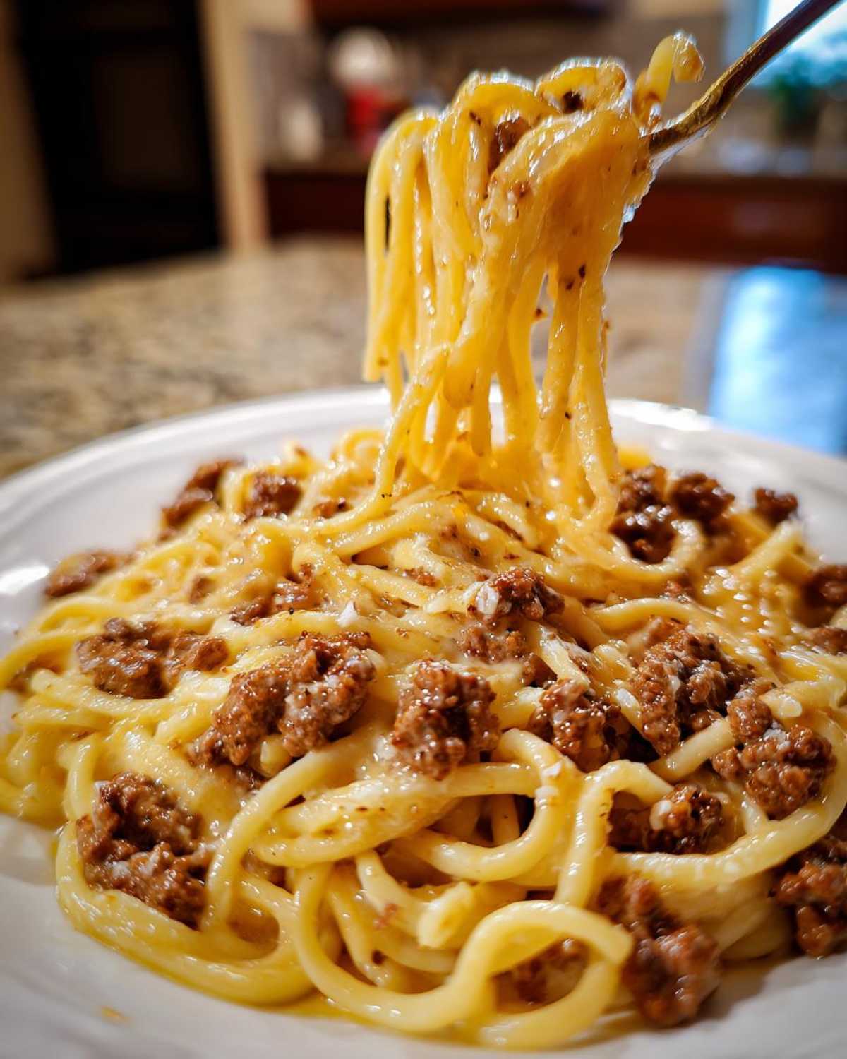 A fork lifting strands of spaghetti coated in rich sauce and ground beef from a plate of creamy beef pasta.