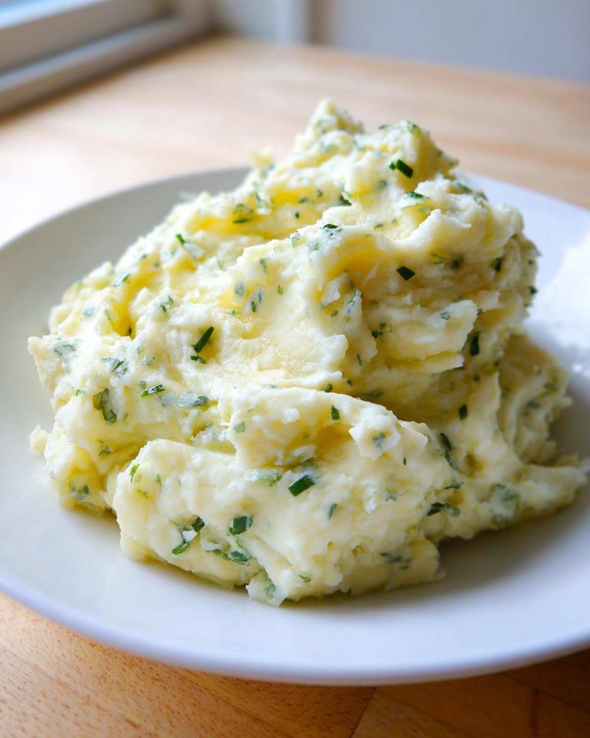 A generous serving of creamy boursin mashed potatoes topped with fresh green chives on a white plate.