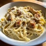 Close-up of creamy chicken fettuccine alfredo pasta topped with grated Parmesan cheese and black pepper.
