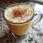 A close-up of creamy homemade eggnog in a clear mug, topped with a dusting of cinnamon.