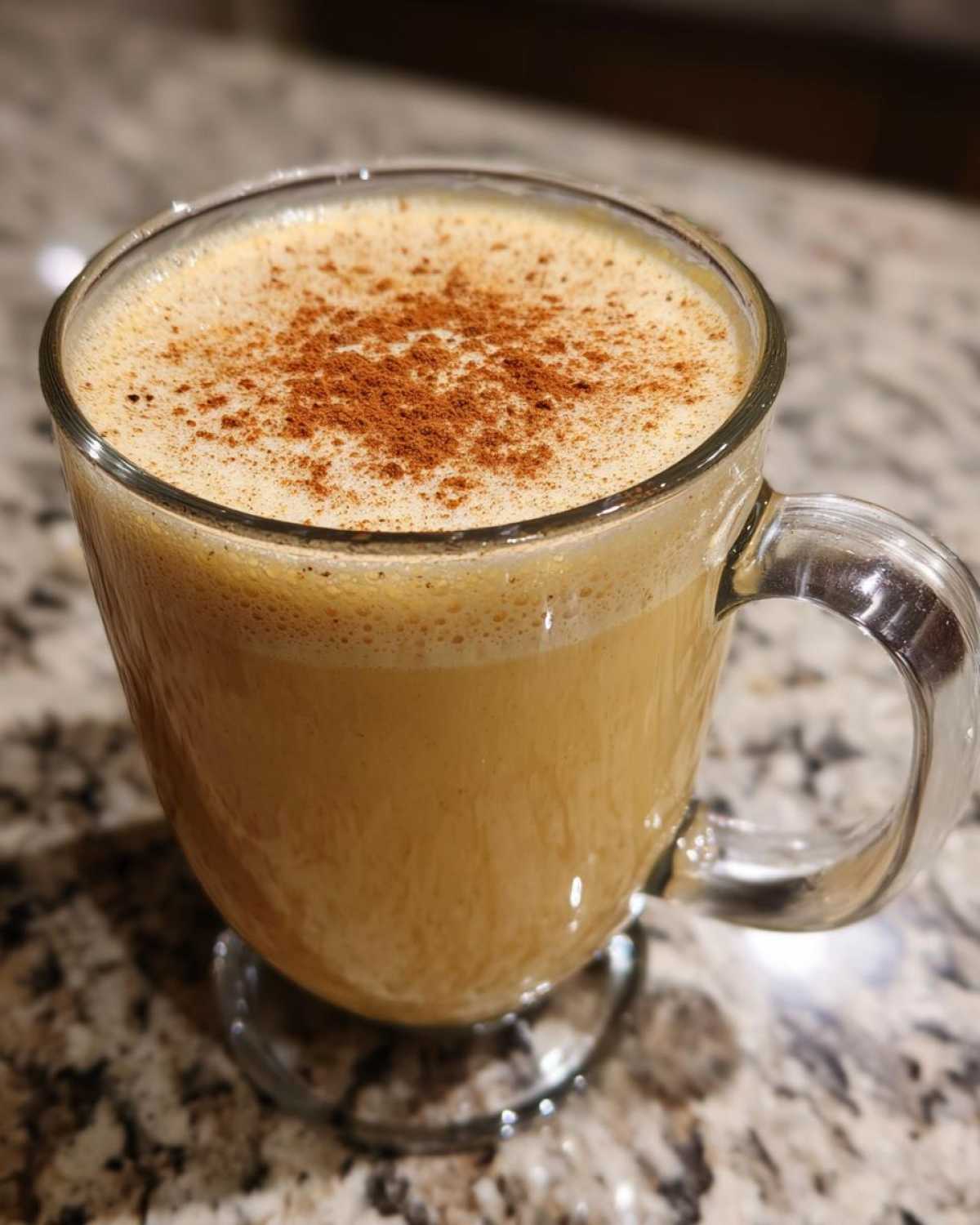 Close-up of a glass mug filled with creamy eggnog, topped with a dusting of cinnamon.