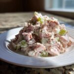 A close-up mound of creamy ham salad recipe mixed with diced celery on a white plate.