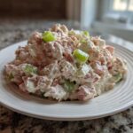A generous scoop of creamy ham salad recipe mixed with diced celery, served on a white plate.