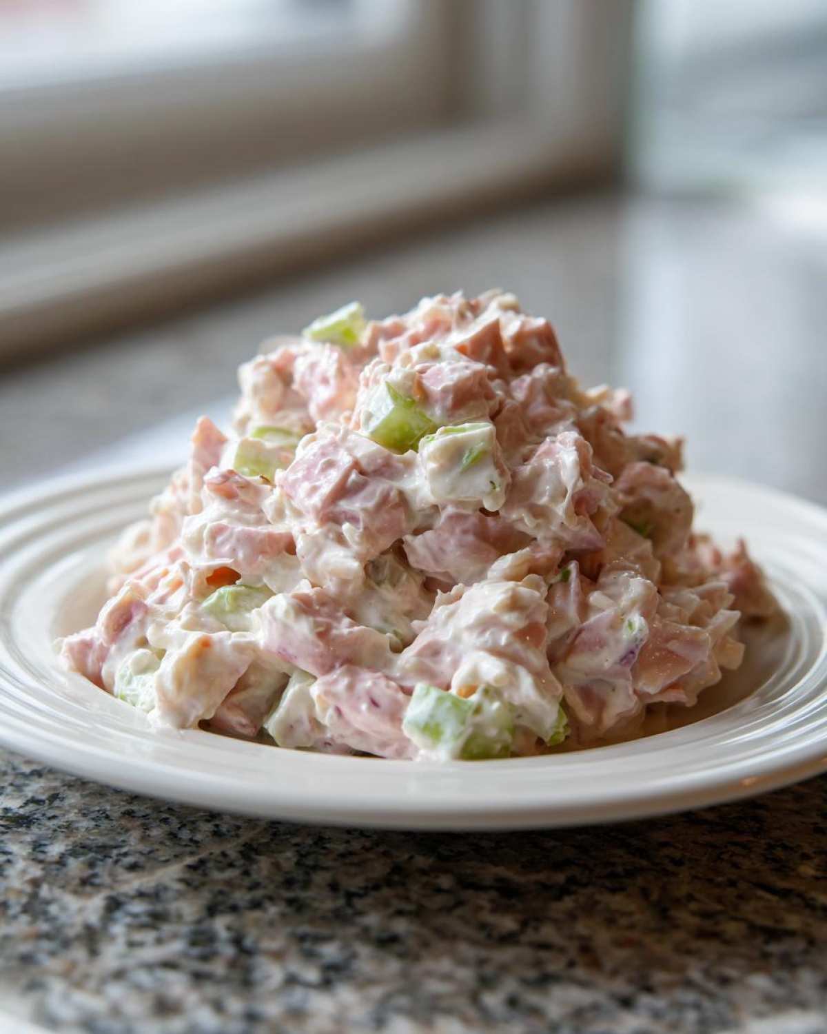A mound of creamy ham salad recipe mixed with diced celery, served on a white plate.