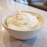 A close-up of thick, creamy horseradish sauce swirled high in a small white bowl.