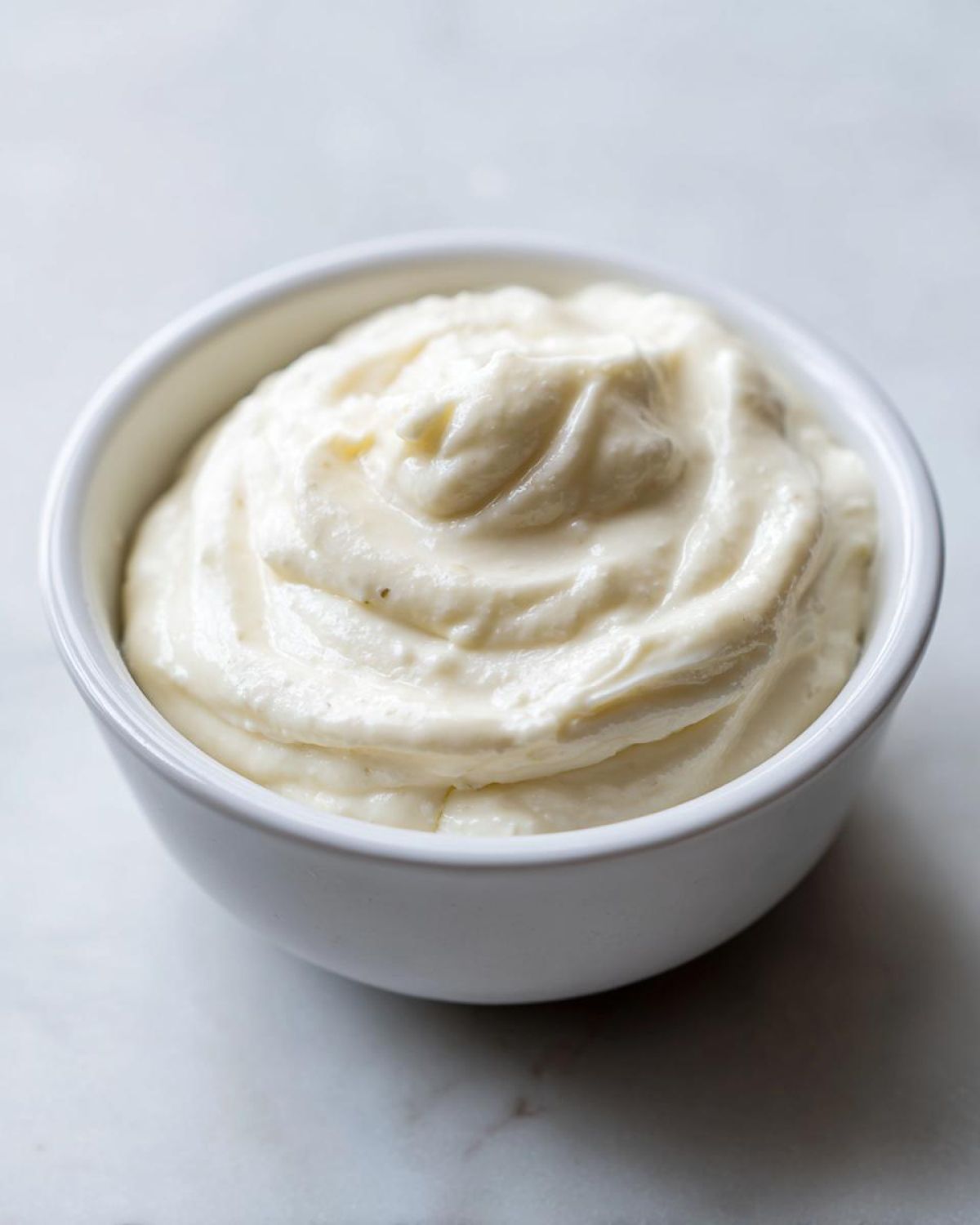 A close-up of thick, creamy horseradish sauce swirled perfectly in a small white bowl.