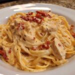 Close-up of creamy Marry Me Chicken Pasta featuring fettuccine, chicken pieces, and sun-dried tomatoes in a white bowl.