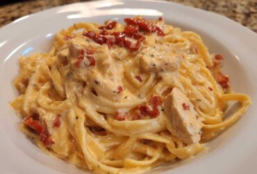 Close-up of creamy Marry Me Chicken Pasta featuring fettuccine, chicken pieces, and sun-dried tomatoes in a white bowl.