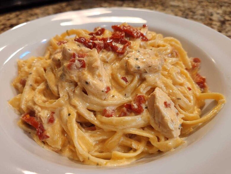 Close-up of creamy Marry Me Chicken Pasta featuring fettuccine, chicken pieces, and sun-dried tomatoes in a white bowl.