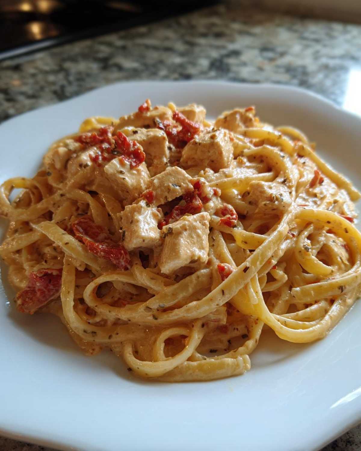 Close-up of a serving of Marry Me Chicken Pasta featuring fettuccine coated in creamy sauce, diced chicken, and sun-dried tomatoes.