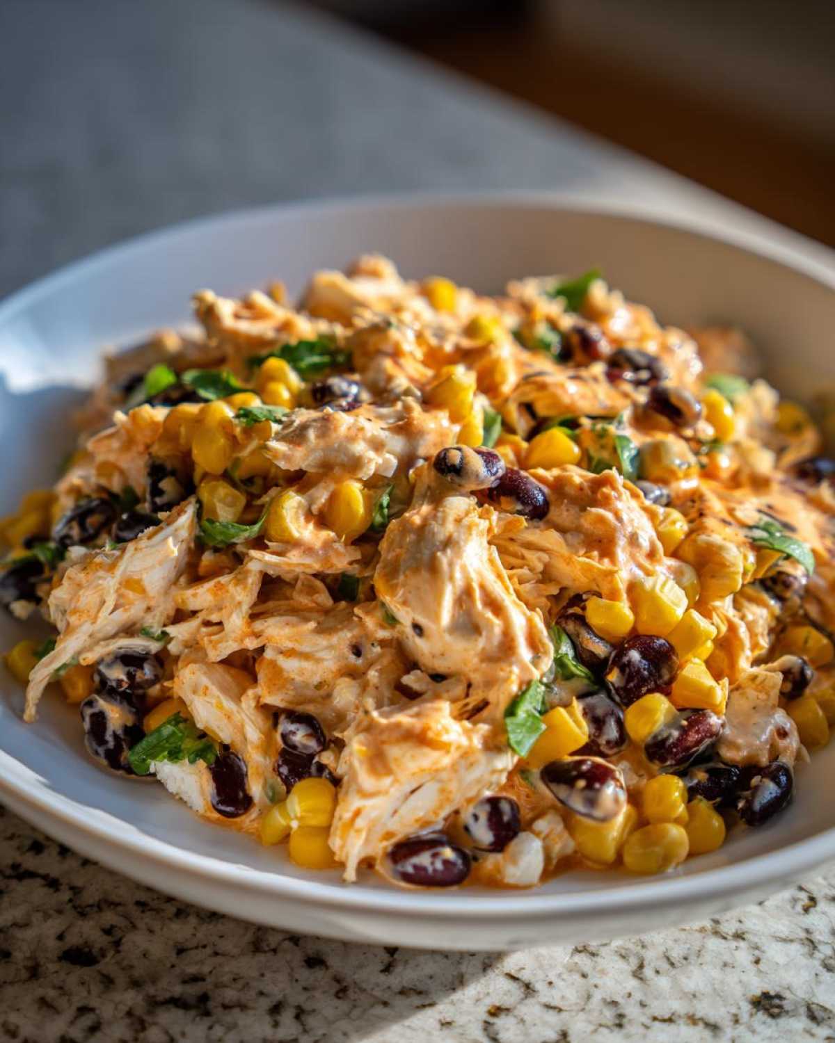 Close-up of creamy southwest chicken salad featuring shredded chicken, black beans, and corn in a white bowl.