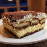A decadent slice of homemade tiramisu recipe featuring layers of cream, soaked ladyfingers, and dusted with cocoa powder.