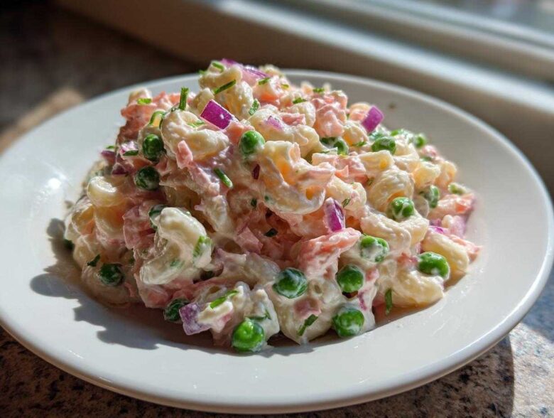 A close-up of creamy Tuna Pasta Salad mixed with elbow macaroni, green peas, red onion, and herbs on a white plate.