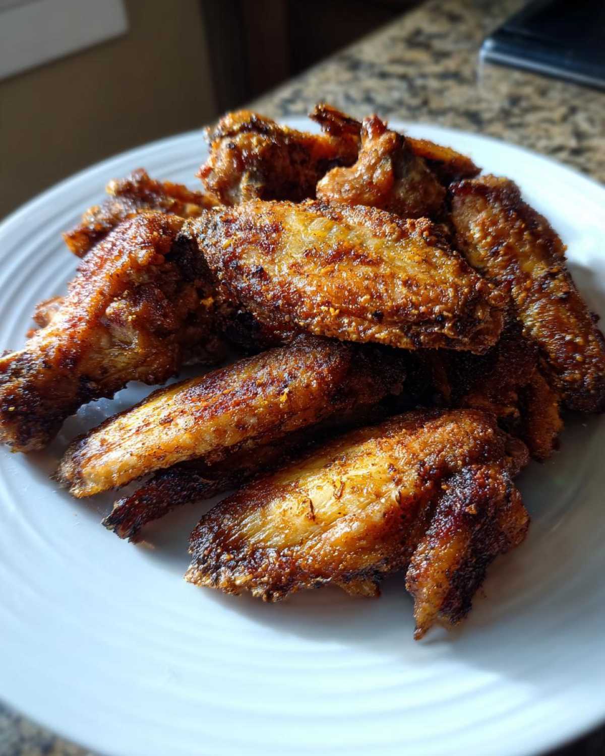 A pile of golden brown, crispy air fryer chicken wings seasoned perfectly and served on a white plate.