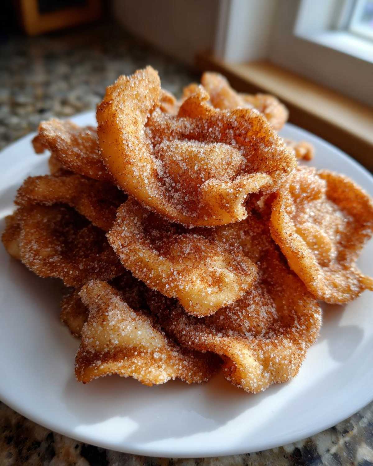 A pile of freshly made, crispy buñuelos generously coated in sparkling cinnamon sugar on a white plate.