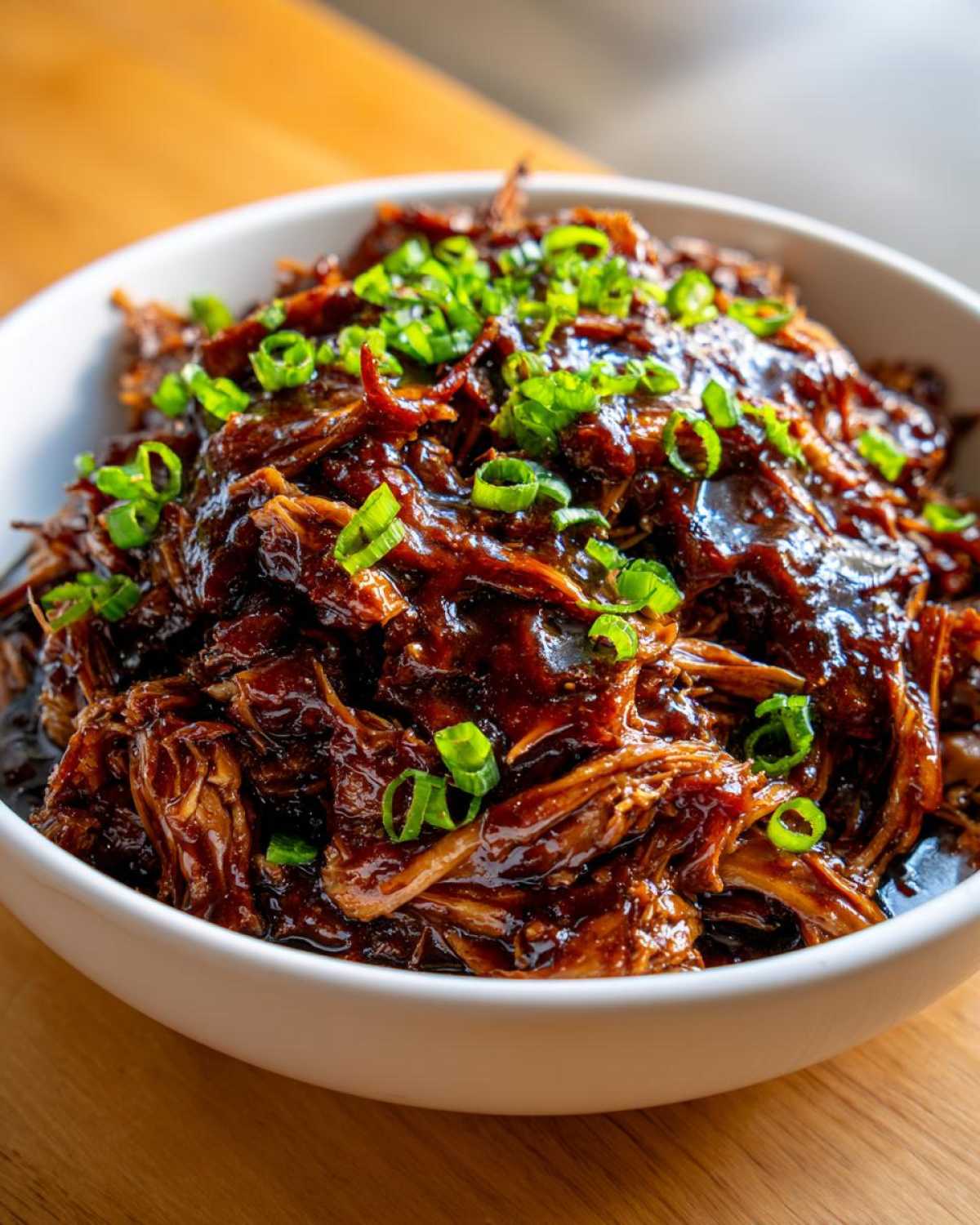 Close-up of shredded crockpot teriyaki chicken coated in thick, dark sauce and topped with green onions.