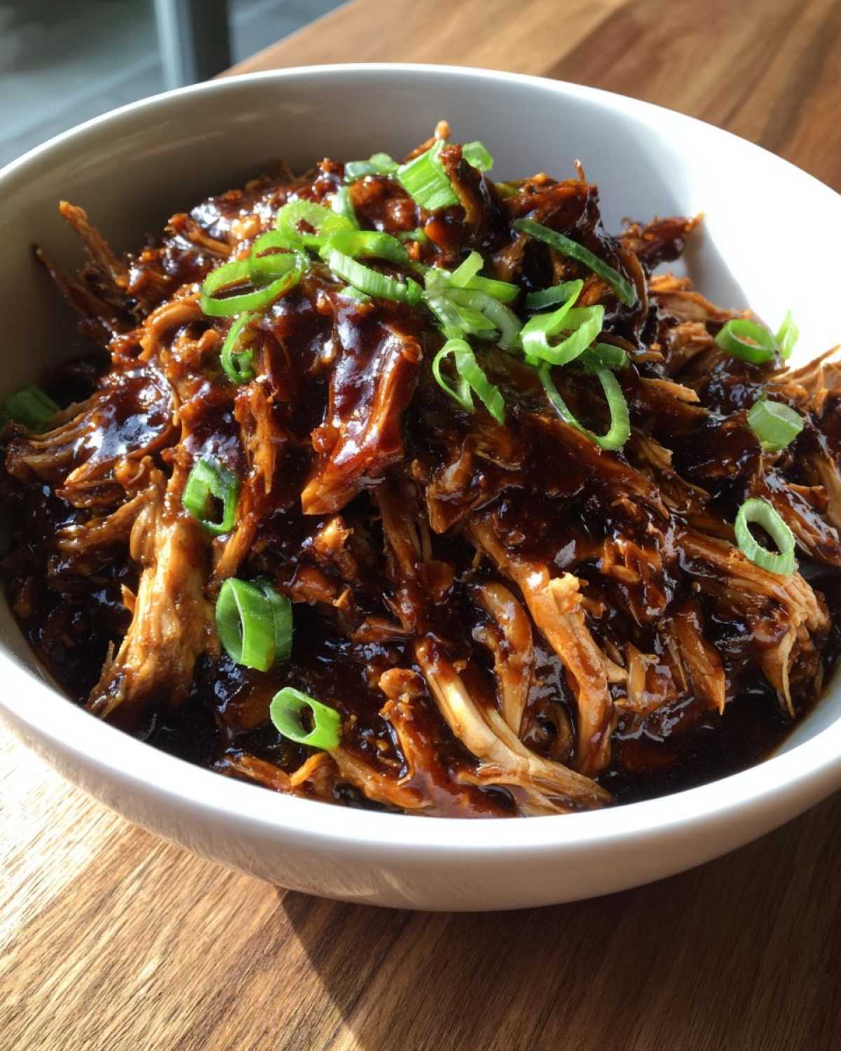 Close-up of shredded crockpot teriyaki chicken coated in dark sauce and topped with sliced green onions.