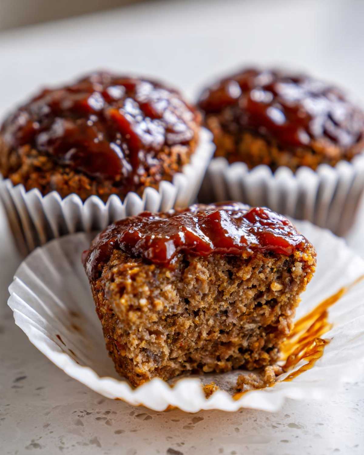 Close-up of a mini meatloaf with a bite taken out, showing the texture and thick glaze on top.
