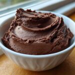 A close-up of thick, dark brown, whipped chocolate dip served in a small white bowl.