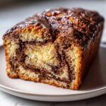 A close-up of a freshly baked chocolate babka loaf with rich chocolate swirls and a glossy chocolate glaze on top.