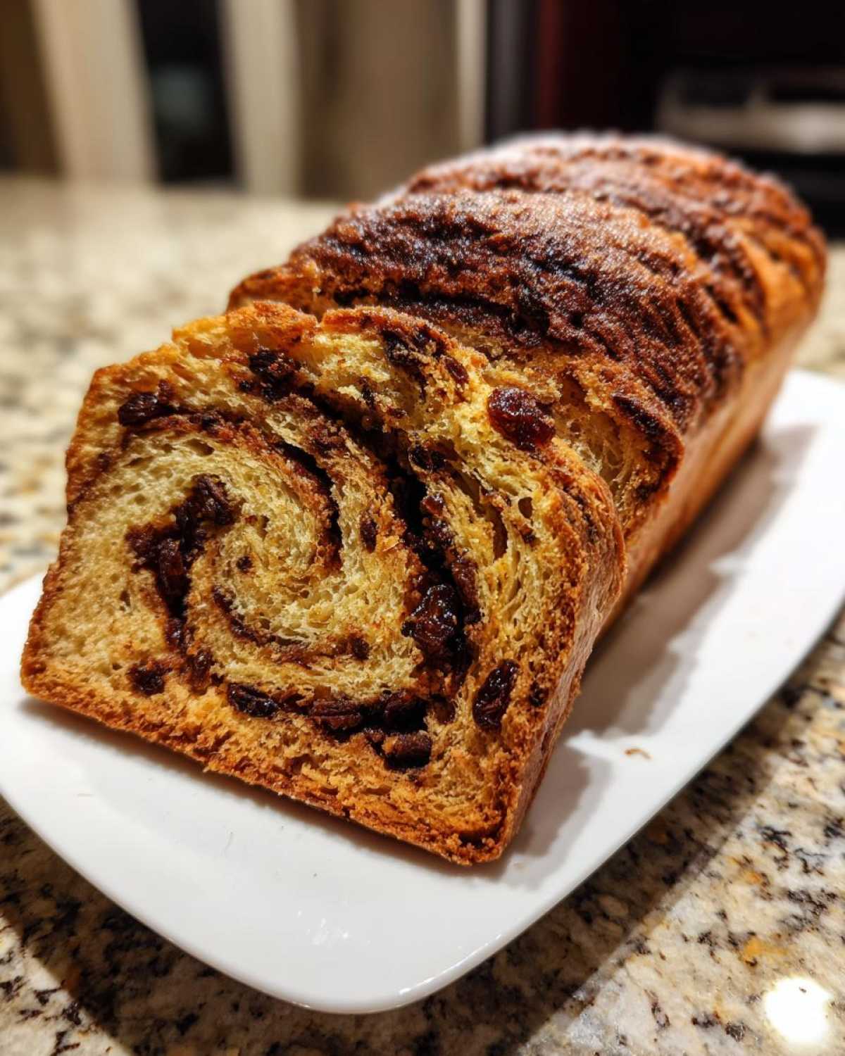 A partially sliced loaf of soft raisin bread showing the swirled cinnamon filling and plump raisins.