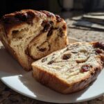 A loaf of soft raisin bread, partially sliced, showing the swirl of cinnamon and plump raisins inside.