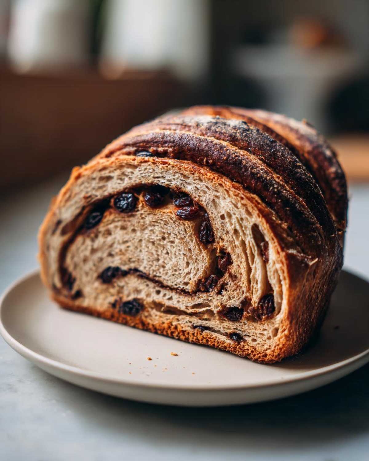 A thick slice of soft, homemade raisin bread with a dark, crusty top resting on a light plate.