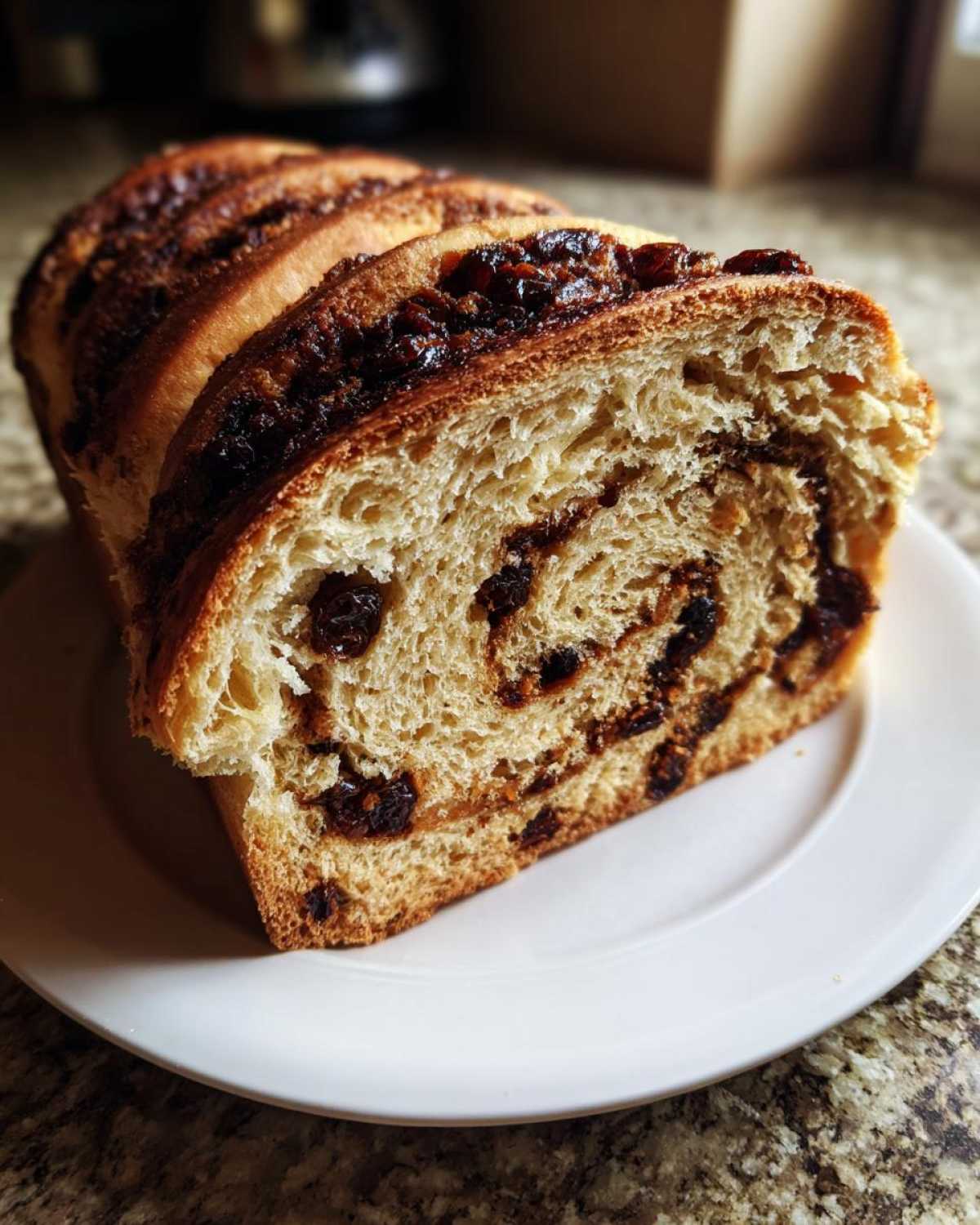 Close-up of a thick slice of soft raisin bread showing the swirl of cinnamon and plump raisins inside.