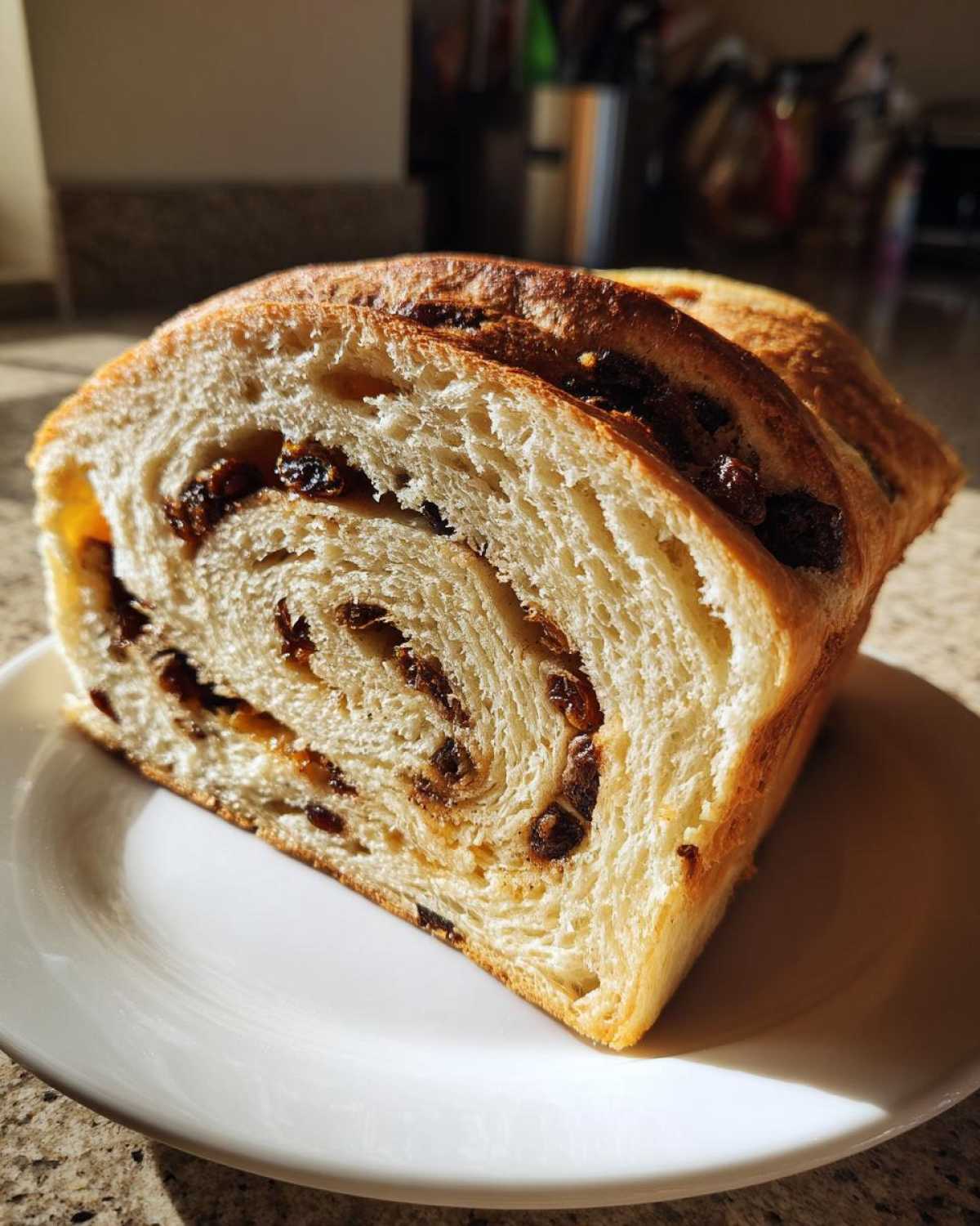 A thick slice of soft, homemade raisin bread showing the beautiful swirl pattern filled with dark raisins.