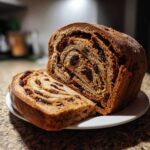 A loaf of homemade raisin bread, sliced to show the beautiful cinnamon swirl and plump raisins inside.