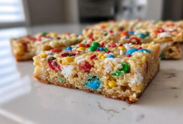 A close-up shot of a thick, chewy christmas cookie bars piece topped with colorful M&Ms and sprinkles.