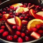 Close-up of rich red holiday sangria filled with cranberries, orange slices, apple chunks, cinnamon sticks, and star anise.