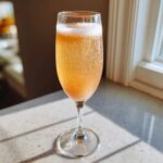 A fizzy, orange-hued bellini recipe cocktail served in a champagne flute on a sunlit countertop.