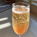A close-up shot of a sparkling, orange-hued bellini recipe served in a champagne flute glass, showing many bubbles.