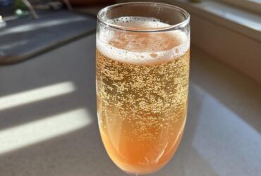 A close-up shot of a sparkling, orange-hued bellini recipe served in a champagne flute glass, showing many bubbles.