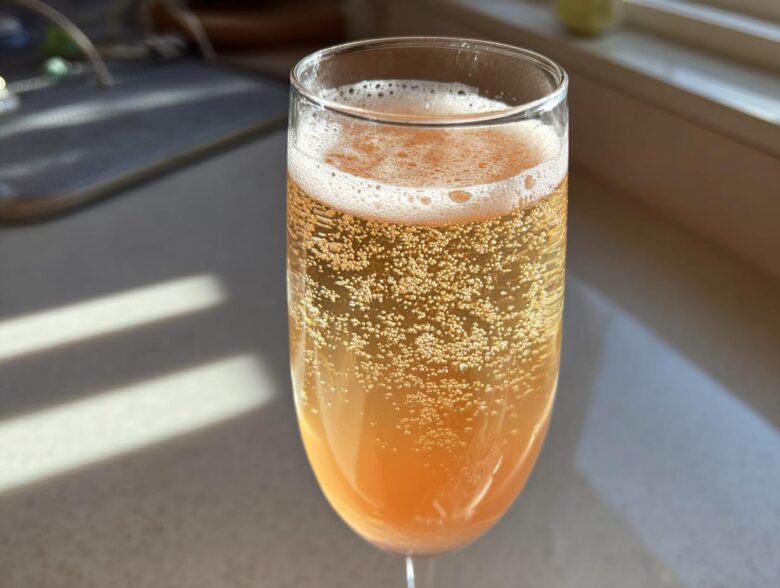 A close-up shot of a sparkling, orange-hued bellini recipe served in a champagne flute glass, showing many bubbles.