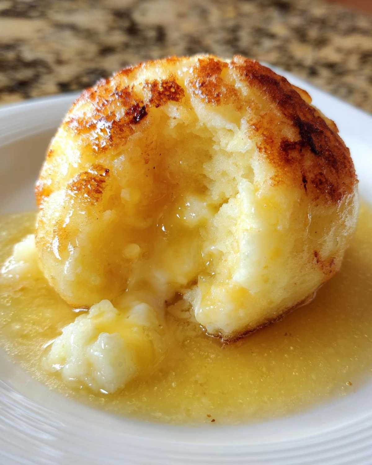 Close-up of a fluffy potato dumplings, browned on the outside and served in a pool of melted butter sauce.