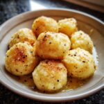 Close-up of golden brown potato dumplings tossed in melted butter and sprinkled with pepper.