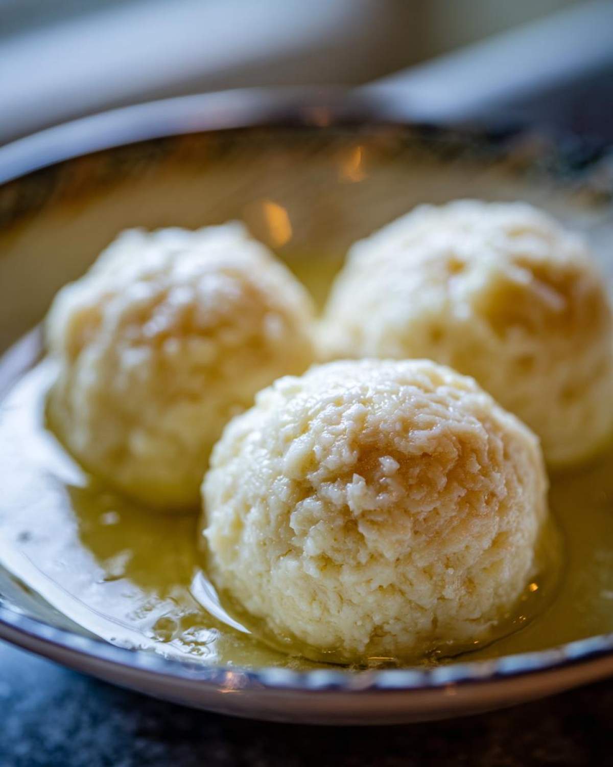 Close-up of three freshly made potato dumplings resting in melted butter in a decorative bowl.