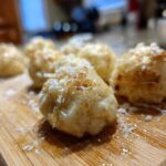 Close-up of several golden brown potato dumplings sprinkled with grated cheese on a wooden cutting board.