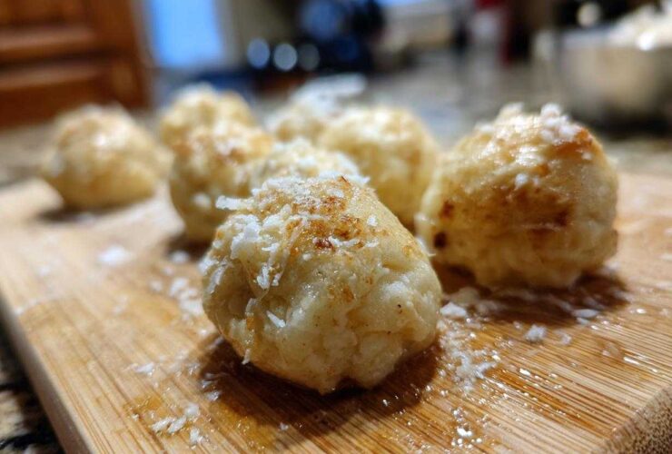 Close-up of several golden brown potato dumplings sprinkled with grated cheese on a wooden cutting board.