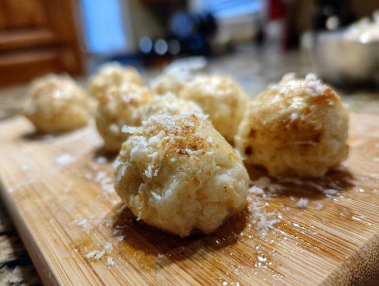 Close-up of several golden brown potato dumplings sprinkled with grated cheese on a wooden cutting board.