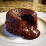 Close-up of a freshly baked lava cake with rich, molten chocolate flowing out onto a white plate.