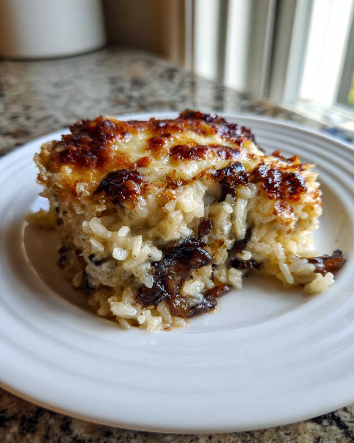 A square serving of baked french onion butter rice with a golden, bubbly, and slightly browned cheese topping.