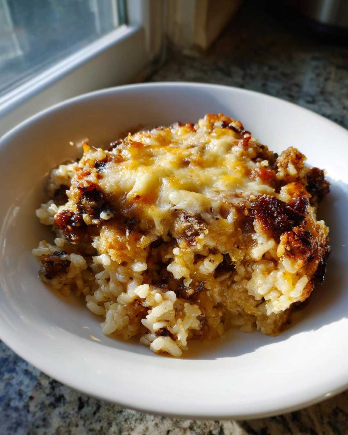 A close-up serving of baked french onion butter rice topped with bubbly, melted cheese in a white bowl.