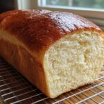 A golden-brown loaf of soft, fluffy condensed milk bread resting on a wire cooling rack.