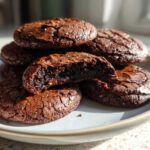 A stack of fudgy chocolate brownie cookies, one broken open to show the rich, dark interior.
