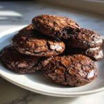 A stack of rich, dark chocolate brownie cookies featuring classic crinkly tops, one cookie has a bite taken out.