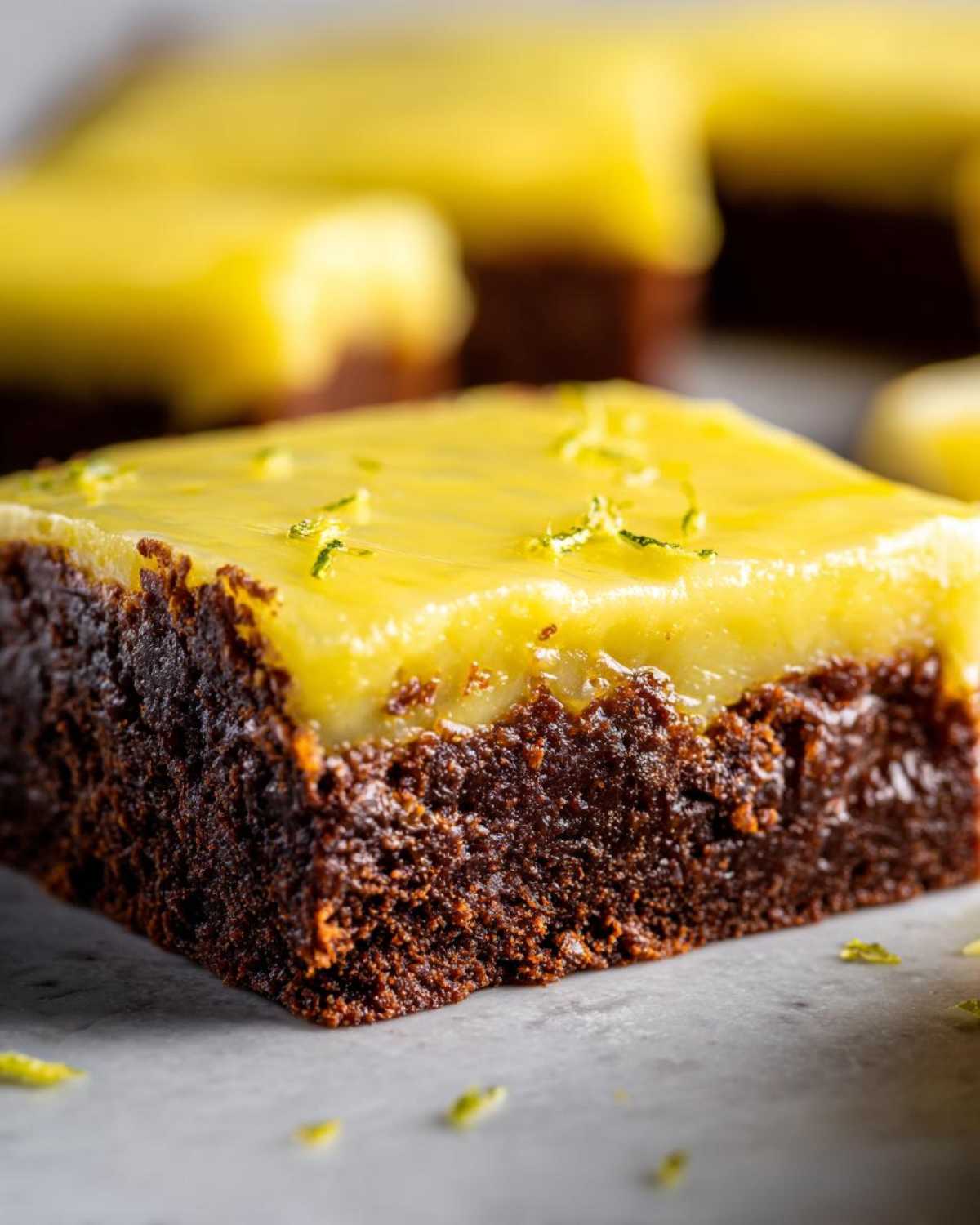 Close-up of a fudgy chocolate Lemon Brownies square topped with a bright yellow lemon glaze and zest.