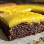 Close-up of a fudgy, dark chocolate Lemon Brownies square topped with a thick, glossy yellow lemon glaze and zest.